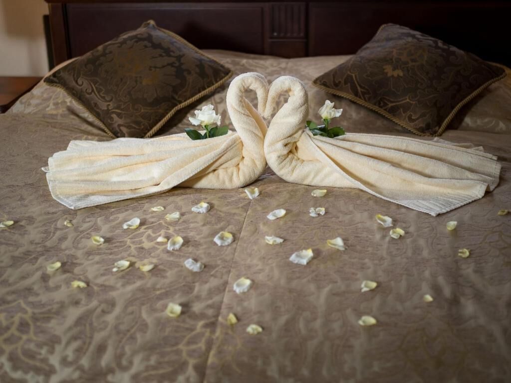 Cama con una decoración de toallas en forma de cisnes, pétalos de flores esparcidos y dos almohadas con diseño estampado.