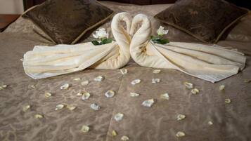 Cama con una decoración de toallas en forma de cisnes, pétalos de flores esparcidos y dos almohadas con diseño estampado.