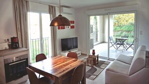 A modern living room with a wooden dining table, a sofa, a TV, and a balcony with outdoor furniture. - Mor102 - Appartement vue mer - 100m de la Plage (Saint-Florent)