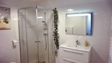 A bathroom with a glass-enclosed shower, a white sink with a mirror above it, and a toilet.