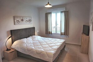 A bedroom with a bed, a nightstand, a TV, a window with curtains, and a wall-mounted artwork. - Mor102 - Appartement vue mer - 100m de la Plage (Saint-Florent)