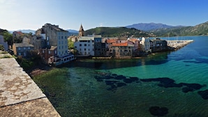 A coastal town with historic buildings, clear blue waters, and mountains in the background. - Mor102 - Appartement vue mer - 100m de la Plage (Saint-Florent)