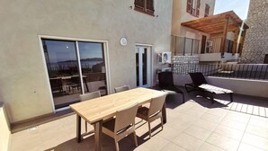 Een terras met een houten tafel en stoelen, een schuifdeur en een klein zitgedeelte met een houten pergola.