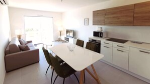Een moderne keuken met witte kastjes, een eettafel en stoelen. De woonkamer heeft een bank en een televisie.