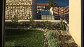 A view of a stone building with a tiled roof, a balcony with a railing, and a clear view of the sea. - Mor310-t2 Neuf vue mer Jardin Jacuzzi 100m Plage (Saint-Florent)