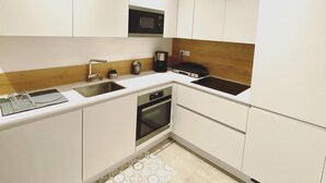 A modern kitchen with white cabinets, a microwave, a coffee maker, and a built-in oven. - Mor405 - T3 Neuf vue mer Panoramique Avec Piscine (Saint-Florent)