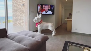 A living room with a sofa, a television mounted on the wall, and a dog statue. - Mor405 - T3 Neuf vue mer Panoramique Avec Piscine (Saint-Florent)