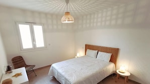 Um quarto com cama, uma cadeira, uma escrivaninha e uma janela.