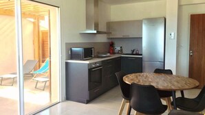 Una cocina moderna con microondas integrado, horno y refrigerador. Hay un área de comedor con una mesa de madera redonda y sillas negras.