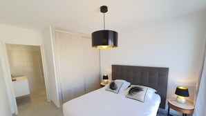 A hotel room with a large bed, two bedside lamps, a grey upholstered headboard, and a modern pendant light. - Mor401 - T5 Neuf Piscine vue mer Panoramique (Saint-Florent)