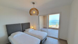 A bedroom with two beds, a ceiling light, and a balcony with a view. - Mor401 - T5 Neuf Piscine vue mer Panoramique (Saint-Florent)