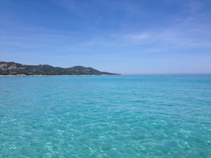 Vista costera con agua turquesa cristalina y una cadena montañosa distante.