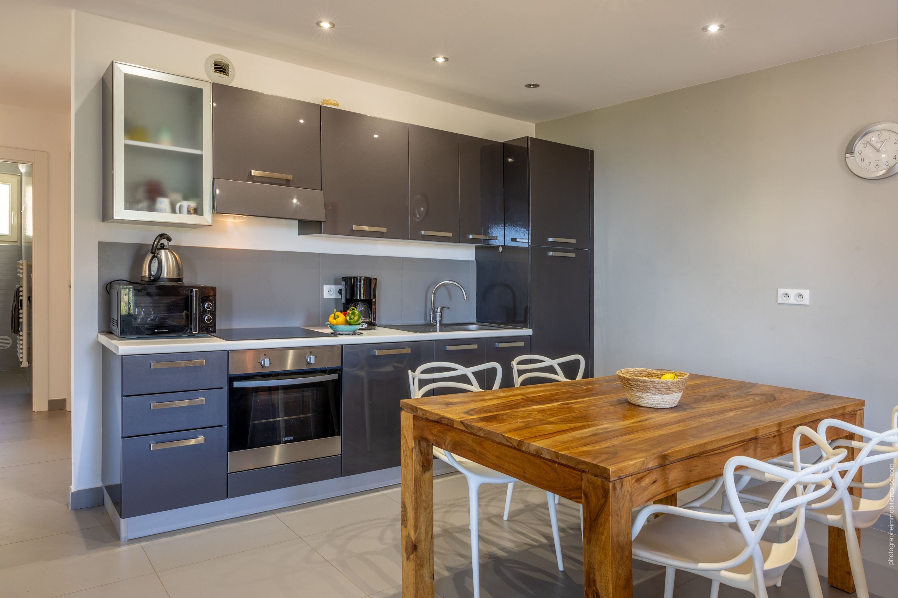 A modern kitchen with grey cabinets, a wooden dining table, and white chairs.