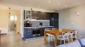 Una cocina moderna con armarios oscuros, una mesa de comedor de madera y sillas blancas.