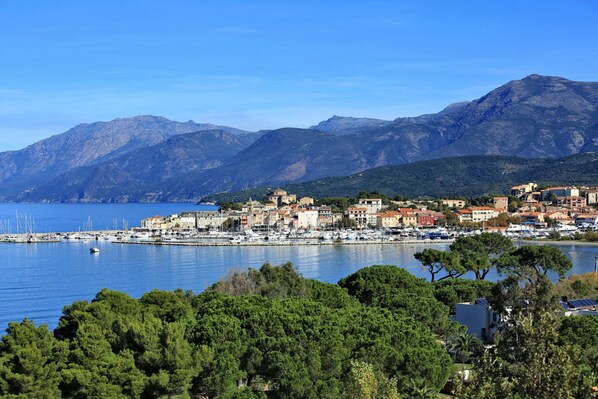 A coastal town with a marina, buildings, and mountains in the background.