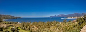 A coastal landscape with a clear view of the sea, mountains, and a town in the distance.