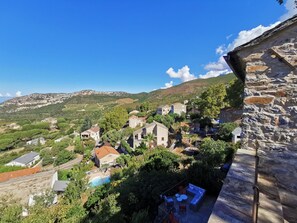 Un pueblo en una ladera con edificios de piedra, una piscina y vistas de las colinas circundantes.