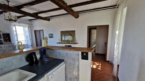 A kitchen with a sink, a coffee machine, and a dishwasher. There is a window with curtains, a wooden ceiling, and a tiled backsplash. - Appartement Palazzo T2 Patrimonio (Patrimonio)