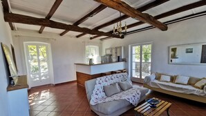 A spacious living area with a high ceiling, exposed wooden beams, a sofa, a coffee table, and a kitchen area with a counter and cabinets. - Appartement Palazzo T2 Patrimonio (Patrimonio)