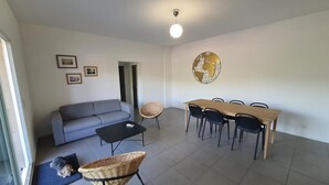 A living room with a grey sofa, a black coffee table, a wicker chair, a dining table with black chairs, and a globe decoration on the wall. - Appartement T3 Luccia Proche Saint Florent (Oletta)