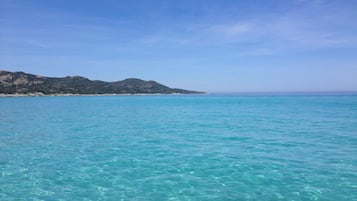 A coastal view with clear turquoise water and a distant mountain range.