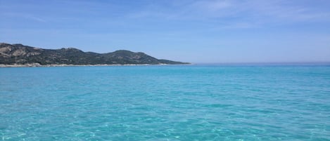 Vista costera con agua turquesa cristalina y una cadena montañosa distante.