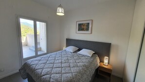 A bedroom with a bed, a nightstand, a wall-mounted picture, and a balcony with a view of greenery. - Appartement T3 Luccia Proche Saint Florent (Oletta)