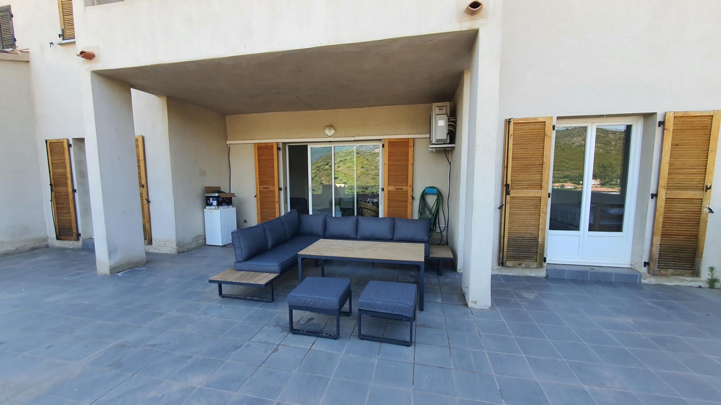 An outdoor seating area with a sofa and table, a refrigerator, and a view of the landscape.