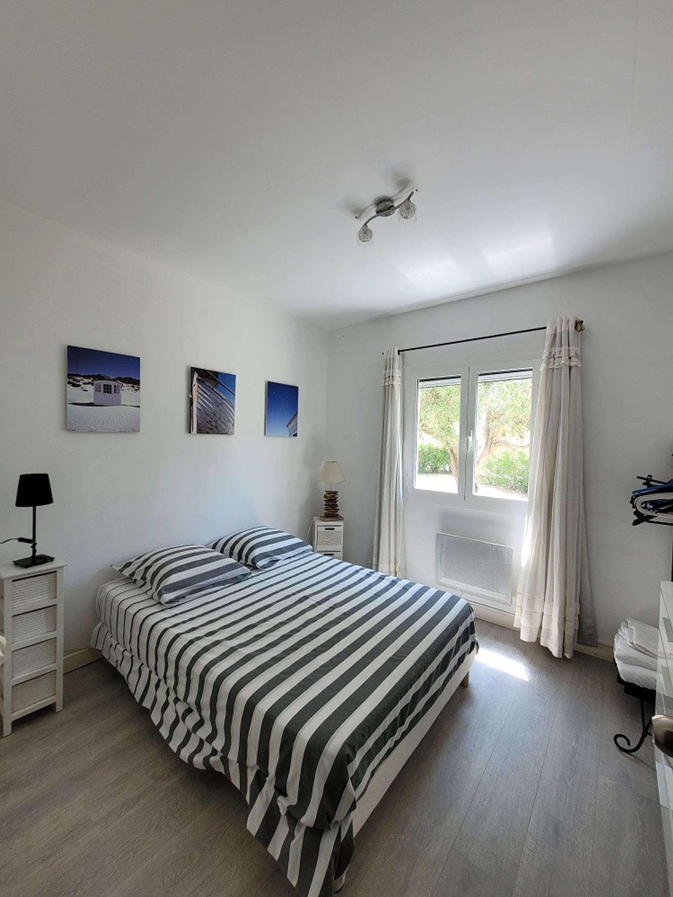 A bedroom with a bed, a bedside table with a lamp, a window with curtains, and wall art.