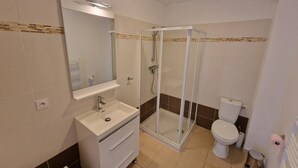 Een moderne badkamer met een douchecabine van glas, een wit wastafelmeubel met een spiegel erboven en een toilet.