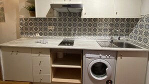 Eine kompakte Küche mit weißen Schränken, einer integrierten Waschmaschine und einer Spritzschutzwand mit Muster.