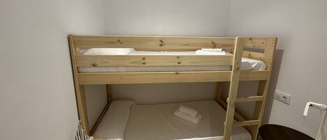 A bunk bed room with a patterned floor, a small table with a flag, and a trash bin.
