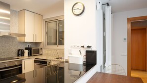 A modern kitchen with stainless steel appliances, a wooden dining table, and a wall-mounted clock.