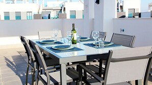 Un espace de restauration aménagé sur le toit, avec une table dressée pour quatre personnes, entourée de chaises, et une bouteille de vin posée sur la table.