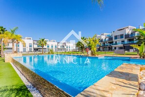 A swimming pool with a stone border, surrounded by a well-maintained lawn and palm trees. - Casa Rosa in Guardamar (Guardamar del Segura)