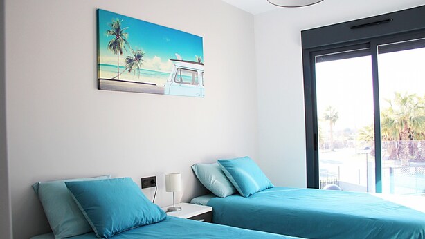 Une chambre d’hôtel avec deux lits, un tableau représentant une scène de plage et une grande fenêtre donnant sur des palmiers.
