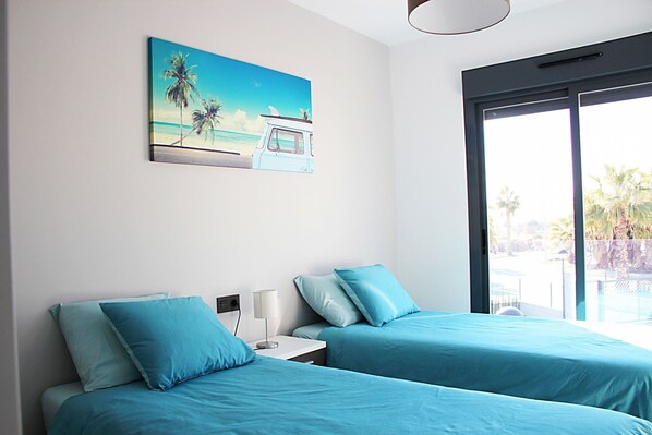 A hotel room with two beds, a painting of a beach scene, and a large window offering a view of palm trees.