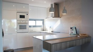 Une cuisine moderne avec des meubles blancs, un four encastré, un évier et des luminaires suspendus.