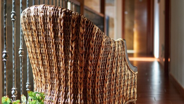 A wicker chair in a hallway with wooden flooring and a stone wall.
