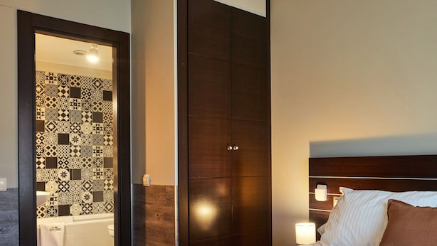 A modern hotel room with a large bed, a wooden wardrobe, a bathroom with patterned tiles, and a nightstand with a lamp. - AV Soterra a 3B in Vila (Ávila)
