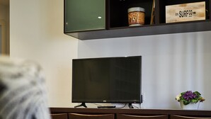 Un salon moderne avec un téléviseur à écran plat, un meuble en bois foncé et une petite plante sur la droite.