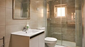 Une salle de bain moderne dotée d’une douche à parois de verre, de toilettes et d’un meuble-lavabo avec un miroir.