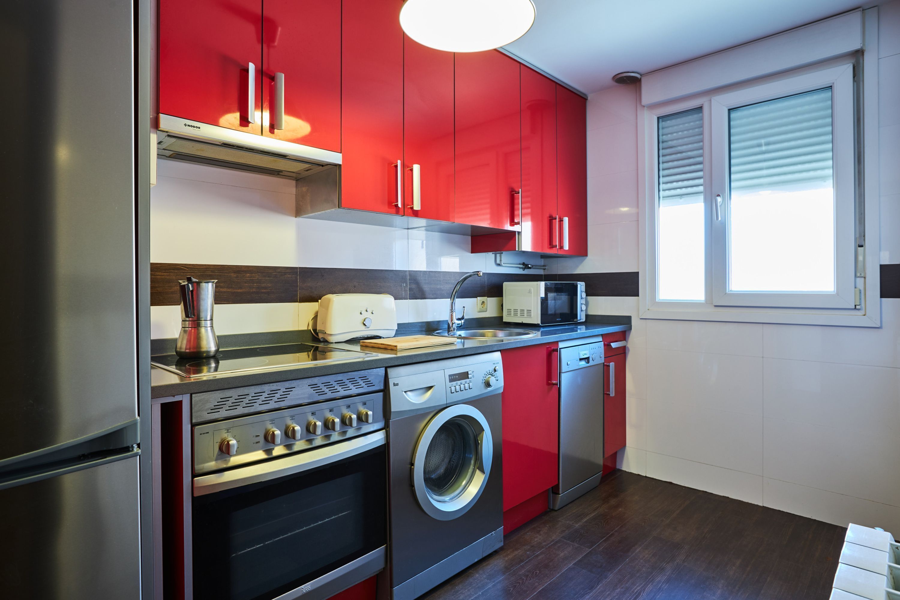 Une cuisine moderne dotée d’appareils électroménagers en acier inoxydable, de meubles de rangement rouges et d’un lave-linge encastré.