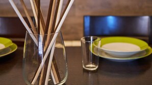 Ein Esstisch mit einer klaren Glasvase, gefüllt mit Holzstielen, einem kleinen Glas und grünen Tellern.