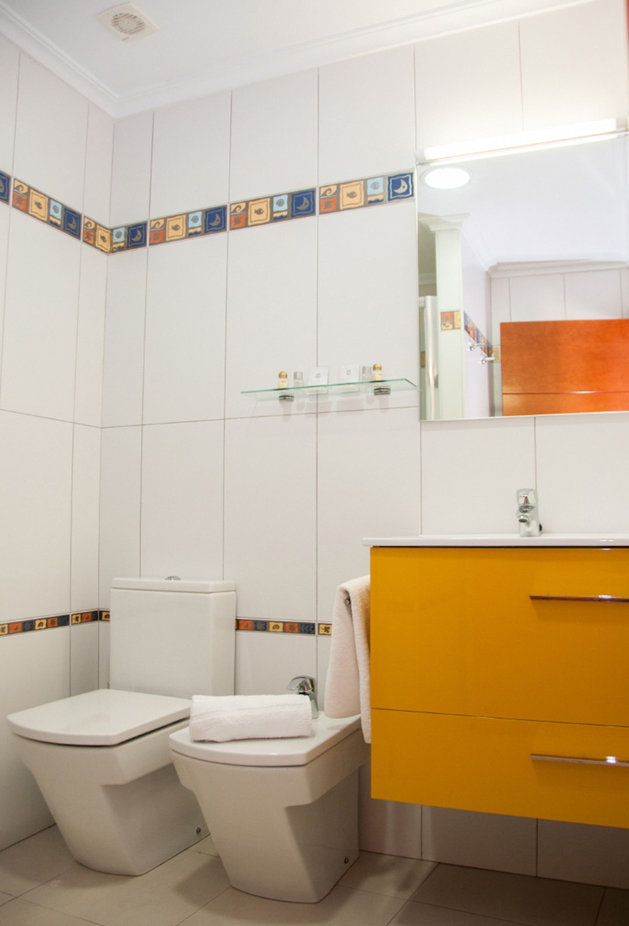 A bathroom with two toilets, a yellow sink, and a mirror above the sink.