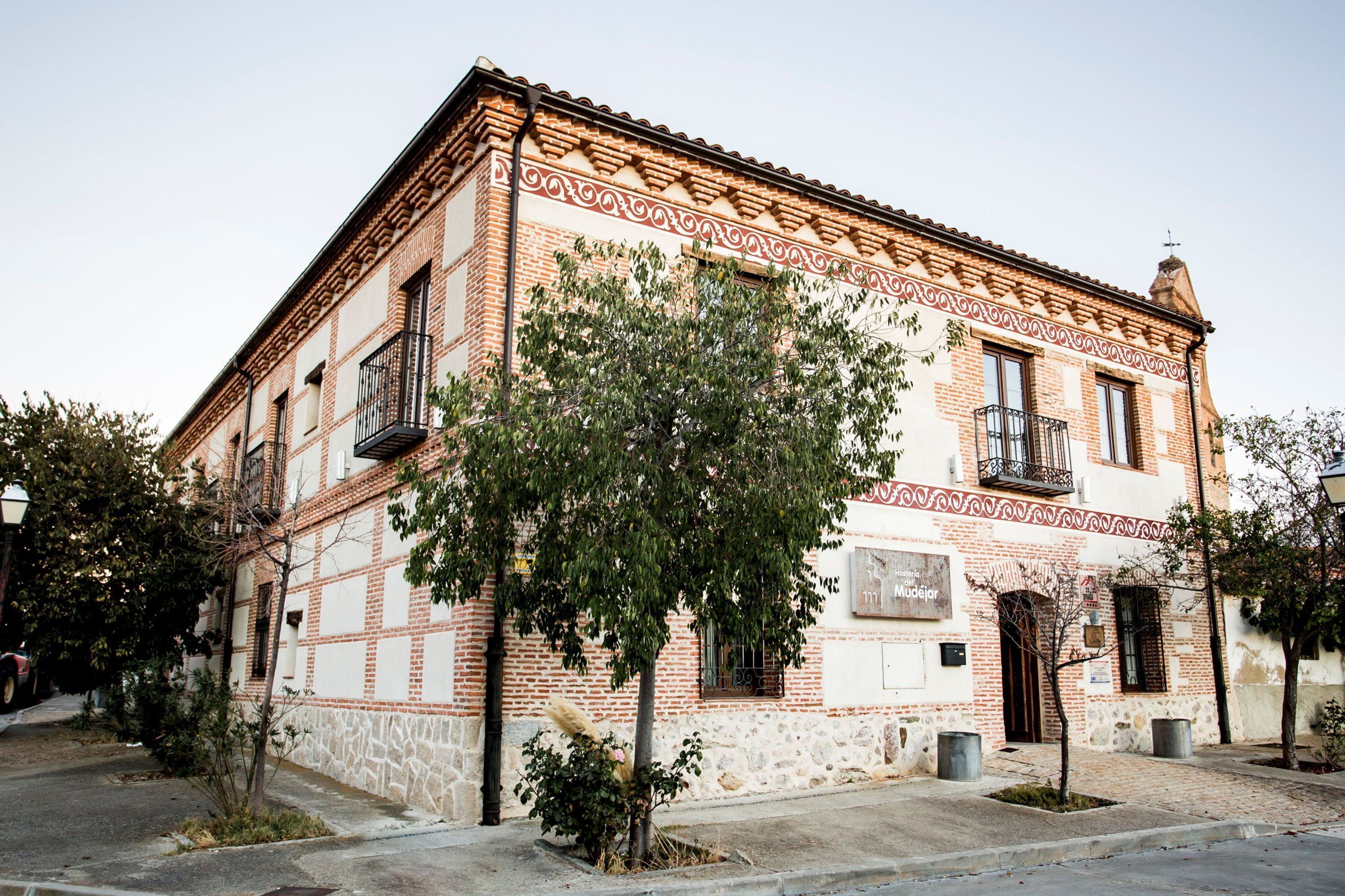 A historic building with a brick facade, a balcony, and a tree in front.