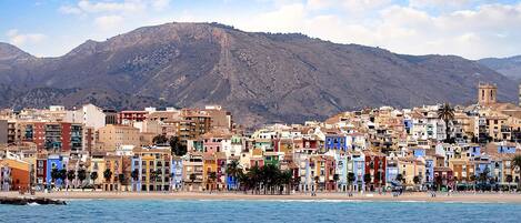 A coastal cityscape with colorful buildings, a beach, and a mountain in the background.