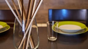Une table à manger sur laquelle se trouve un vase en verre transparent contenant des bâtonnets de bois, un petit verre et des assiettes vertes.