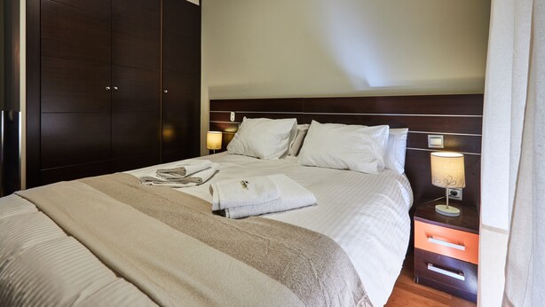 Une chambre d’hôtel avec un grand lit, une armoire, une table de chevet avec une lampe et une petite table de nuit.
