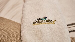 Une serviette blanche, soigneusement pliée et ornée d’un motif brodé, est posée sur le lit.